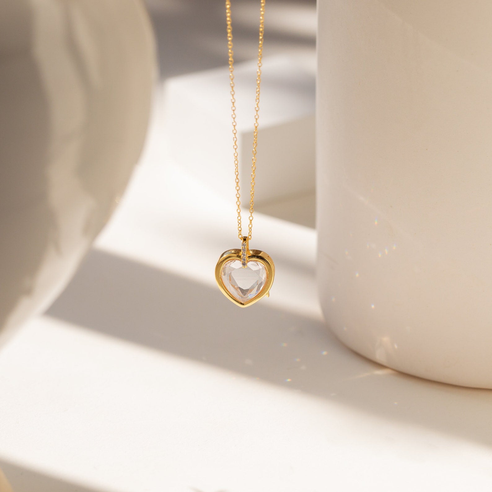 Crystal Locket Necklaces feature a gold chain and heart-shaped pendant, beautifully showcased in soft, natural light against a neutral background.