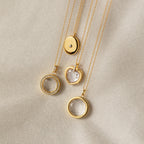 Four Crystal Locket Necklaces with oval, round, and heart-shaped pendants, including a Photo Locket Necklace, elegantly displayed on beige textured fabric.