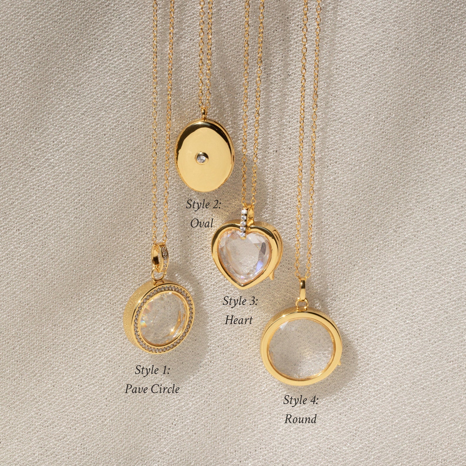 Four gold Crystal Locket Necklaces rest on fabric, each with a unique pendant shape: circle, oval, heart, and round. One locket is perfect for keeping special memories close.