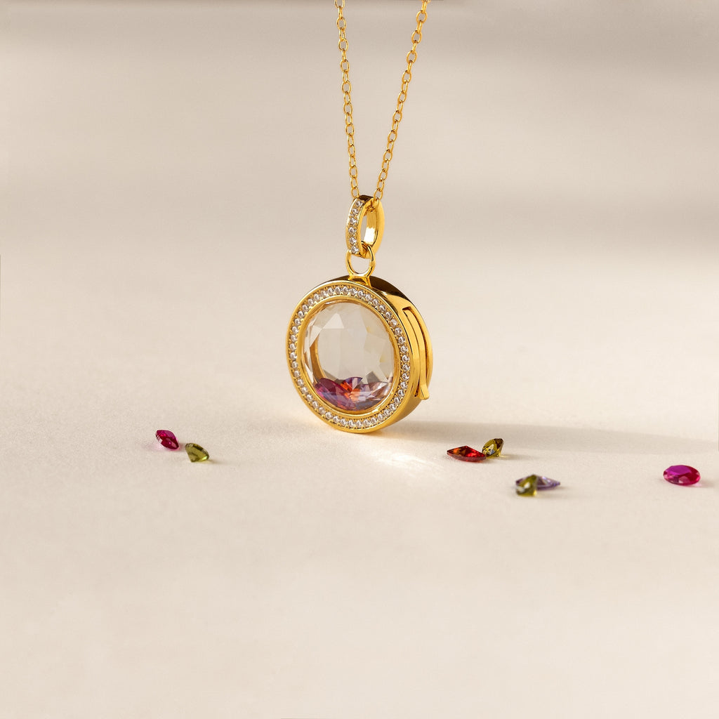 Crystal Locket Necklaces feature a gold pendant with a large faceted gemstone, surrounded by small gems, offering timeless elegance and beautifully displayed on a light surface.