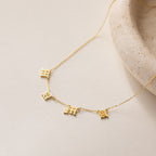 Old English Letter Name Necklace with small dangling charms, shown on a light stone surface—ideal for fans of minimalist jewelry with an edgy vibe.