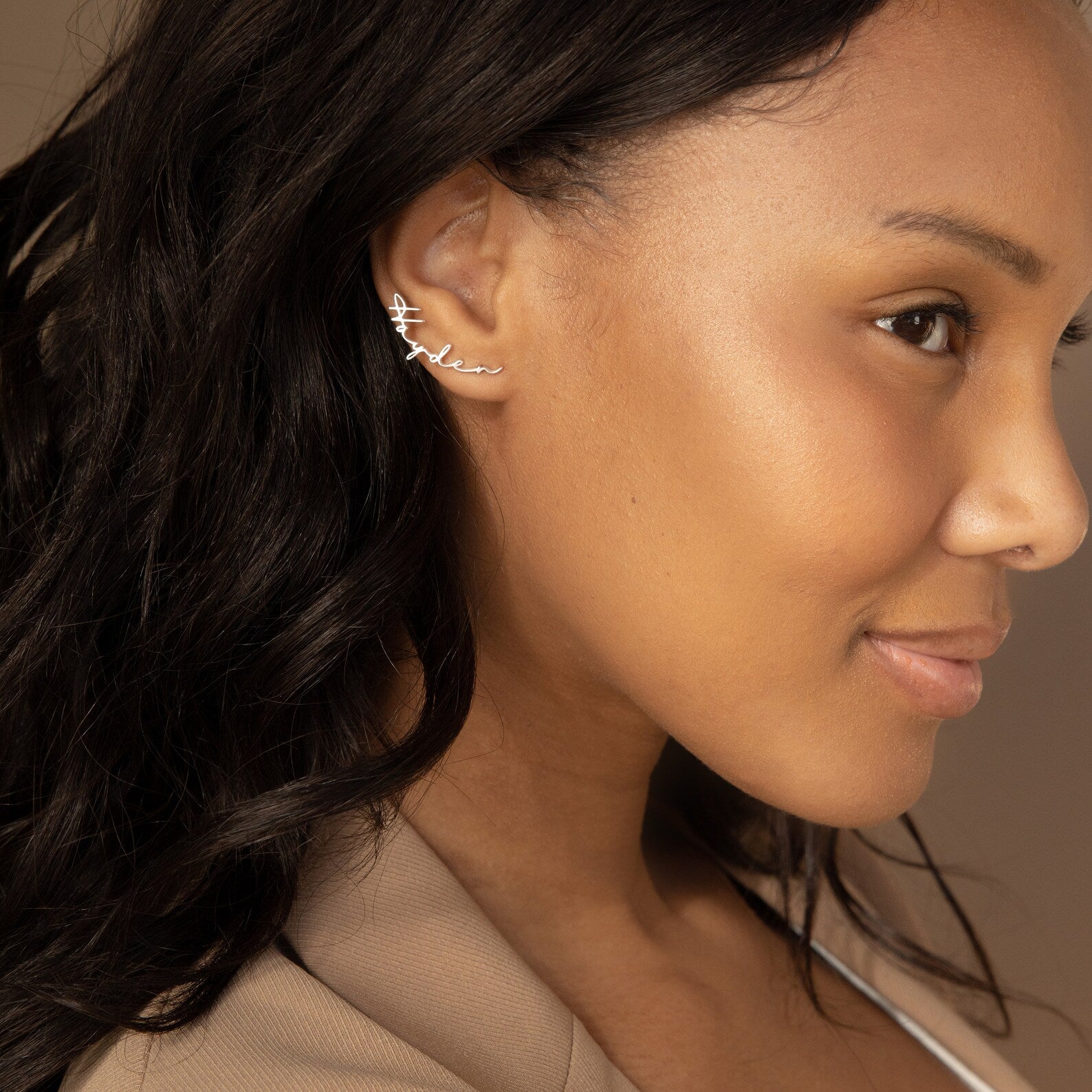 A woman with long dark hair wears Hallie Name Earrings—silver personalized earrings that spell "fearless" in cursive, making them an ideal custom gift.