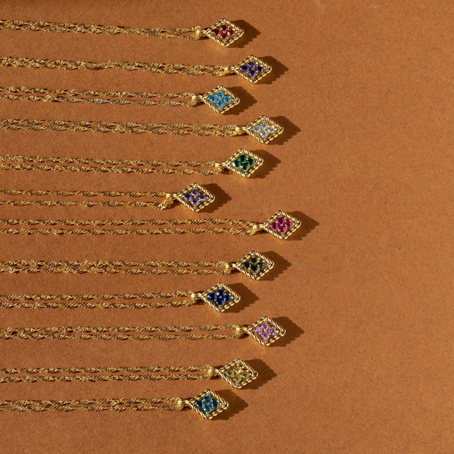 Ten Birthstone Diamond Pendant Necklaces are arranged in a neat diagonal line on a brown background.