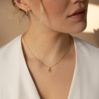 Woman wearing the Birthstone Diamond Pendant Necklace, featuring a gold chain and small square pendant, paired with a white top, shown from the shoulders up.