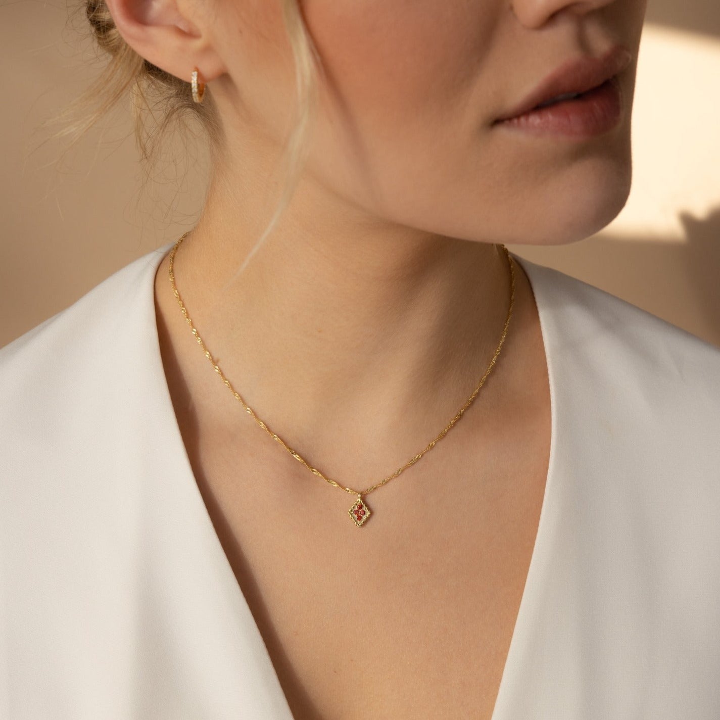 Woman wearing the Birthstone Diamond Pendant Necklace, featuring a gold chain and small square pendant, paired with a white top, shown from the shoulders up.