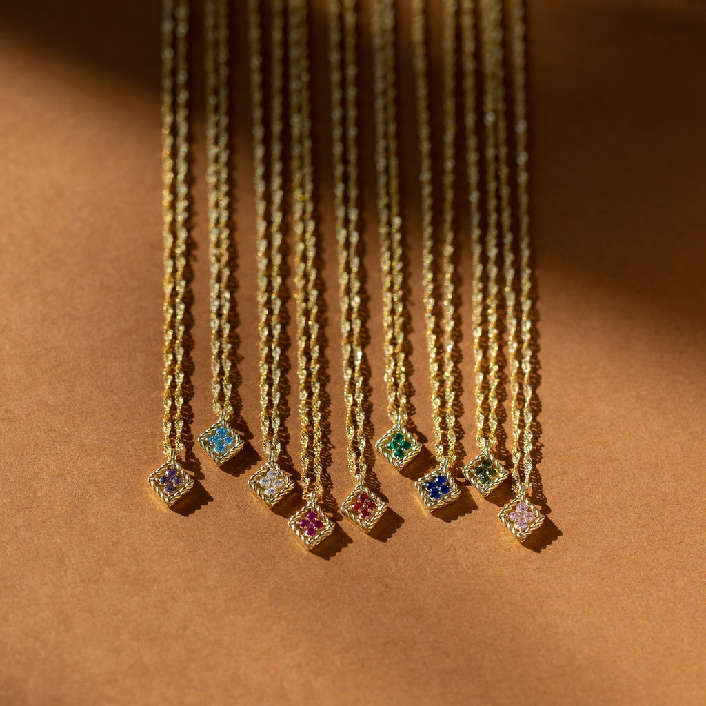 Birthstone Diamond Pendant Necklaces are arranged in a row on a brown background, each showcasing the charm of handcrafted personalized jewelry for those who love gemstone accessories.