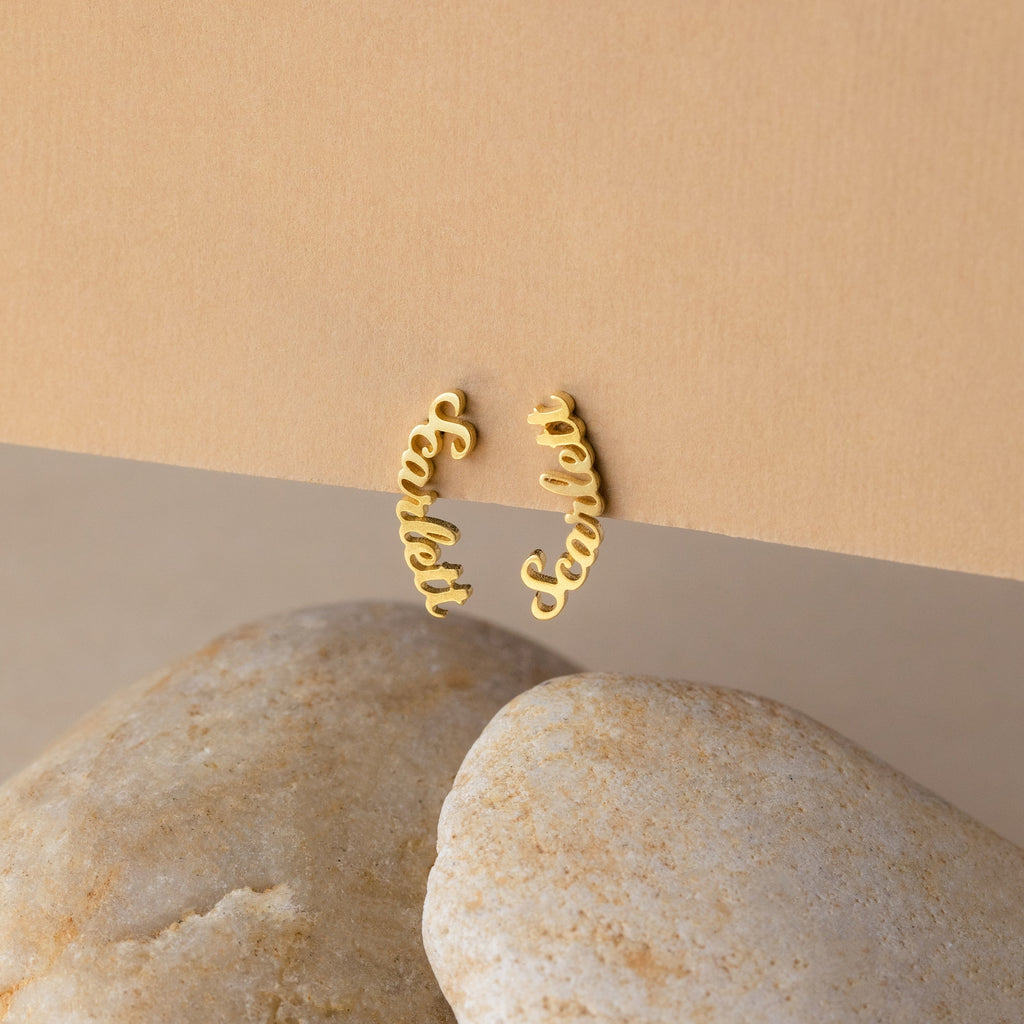 Mellow Name Earrings: Gold hoops featuring the name Scarlett in elegant cursive, styled on a stone and beige background—ideal personalized jewelry for a unique custom gift.