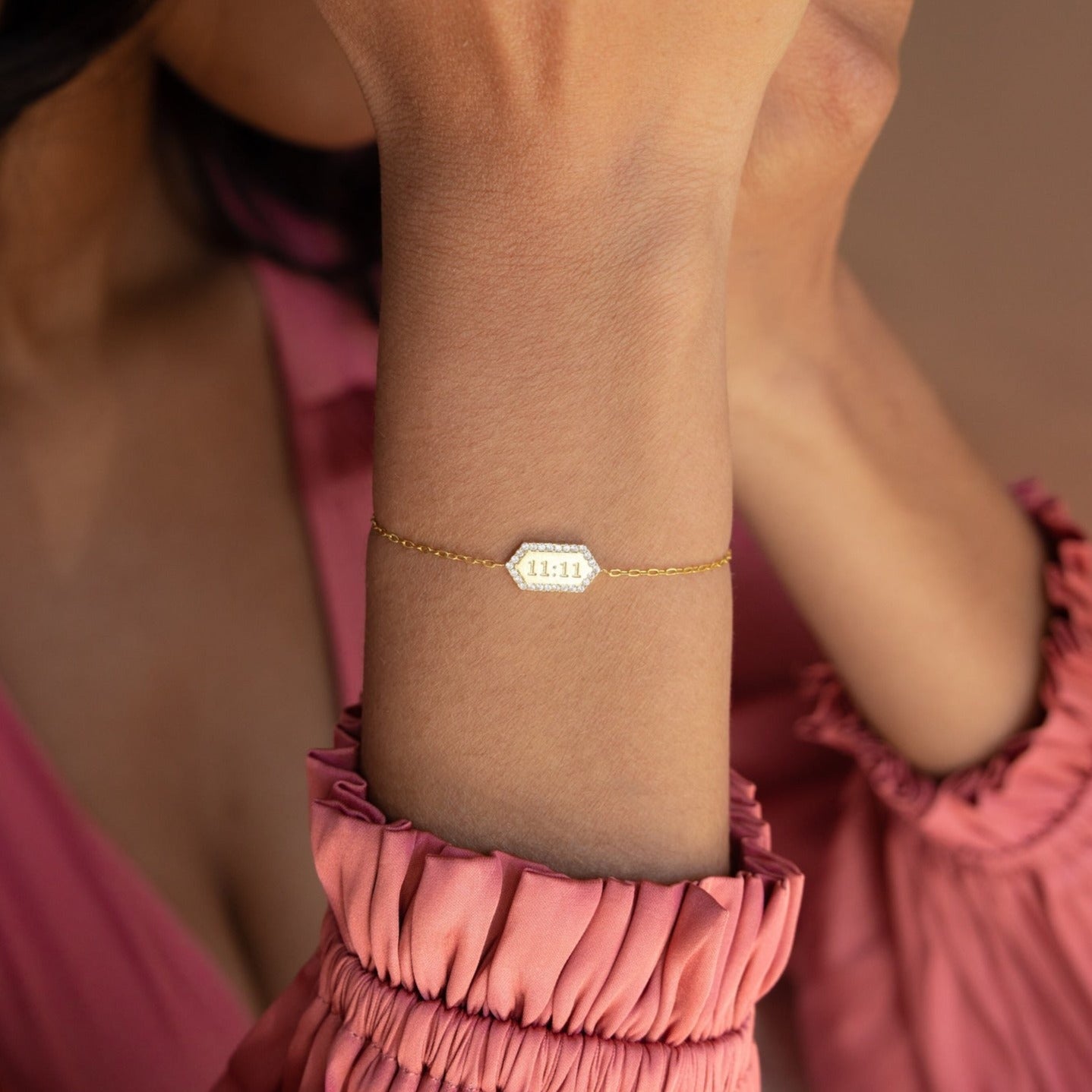 A woman wearing a Custom Pave Hexagon Bracelet engraved with 11:11, paired with a pink ruffled long-sleeve top.