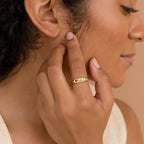 A woman touches her face, wearing the Bold Birthstone Signet Ring adorned with colorful gemstones on her finger.