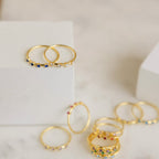 The Space Birthstone Ring, featuring vibrant gemstones set in gold, is elegantly displayed on and around white blocks atop a marble surface.