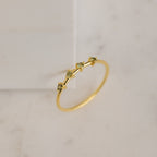 The Space Birthstone Ring features three small yellow gemstones set in a delicate gold band, shown on a light marble surface.
