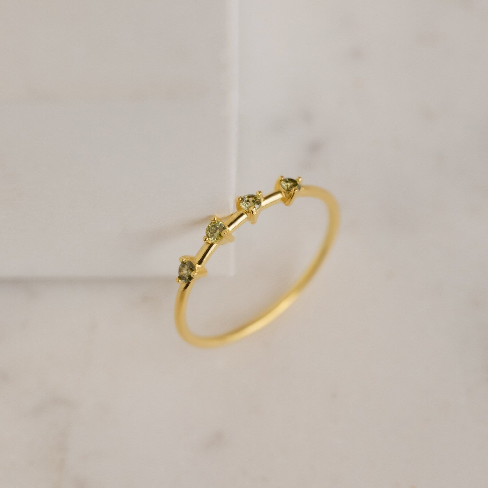 The Space Birthstone Ring features three small yellow gemstones set in a delicate gold band, shown on a light marble surface.