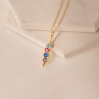 Vertical Pod Birthstone Necklace featuring four vibrant gemstones on a curved pendant, showcased on light stone tiles—a stunning piece of personalized jewelry.