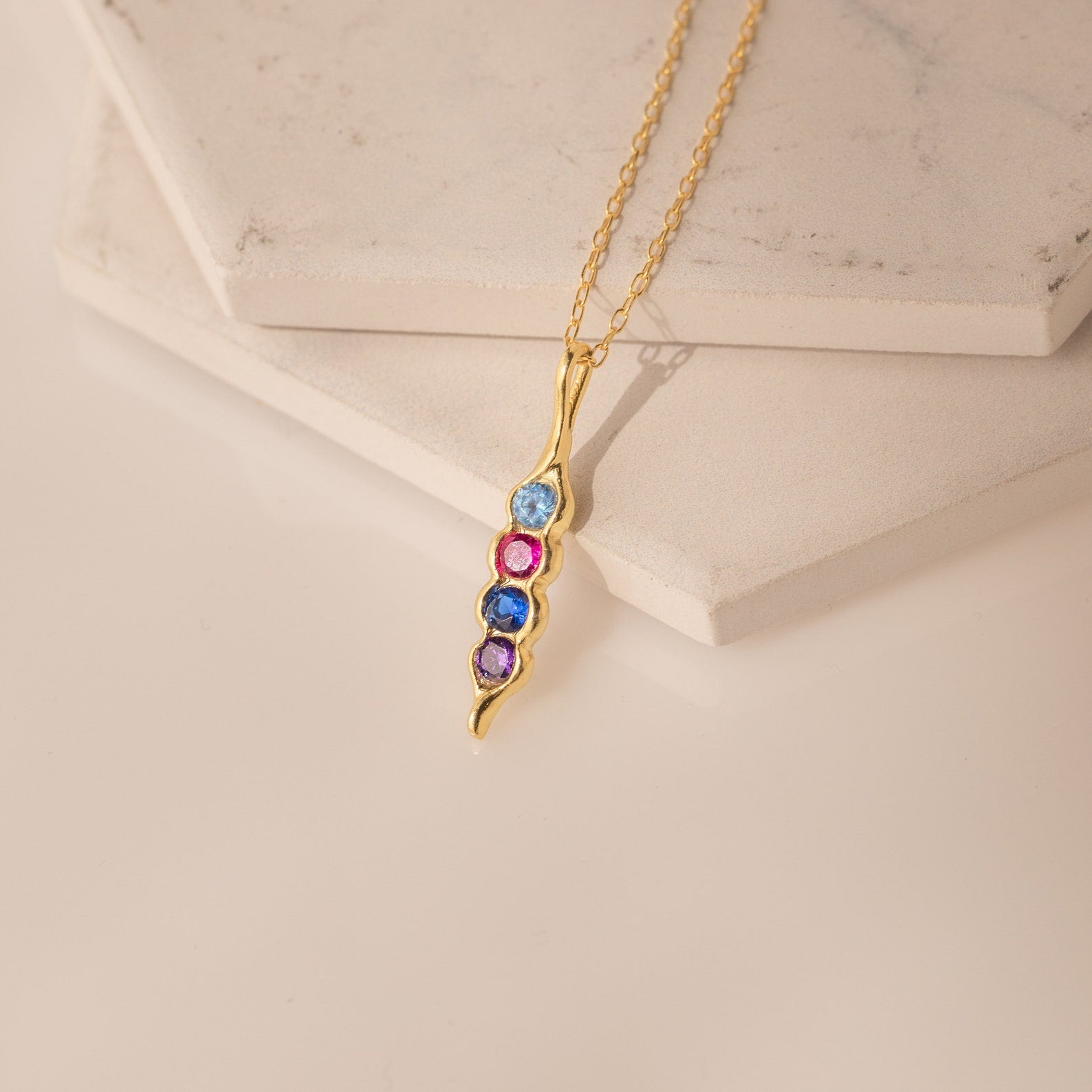 Vertical Pod Birthstone Necklace featuring four vibrant gemstones on a curved pendant, showcased on light stone tiles—a stunning piece of personalized jewelry.