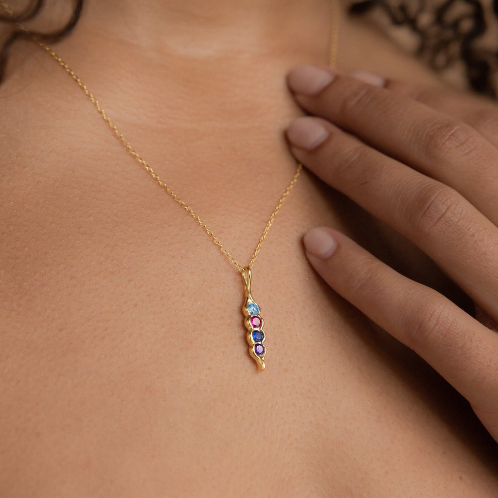 The Vertical Pod Birthstone Necklace features a pendant with colorful gemstones, shown worn by a person touching their collarbone—a stunning and personalized jewelry piece.