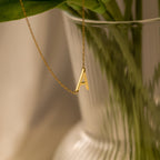 The Mini Sideways Initial Necklace, featuring a gold letter A pendant, drapes elegantly over a clear ribbed glass vase—making it an ideal personalized gift for any occasion.