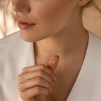 A woman gently holds her Mini Sideways Initial Necklace, featuring a gold letter G pendant—a beautiful personalized accessory.