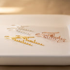 Add a special touch to any look with three pairs of Hallie Dangling Name Earrings in gold, silver, and rose gold—perfect for fans of personalized jewelry. Shown beautifully displayed on a white surface.