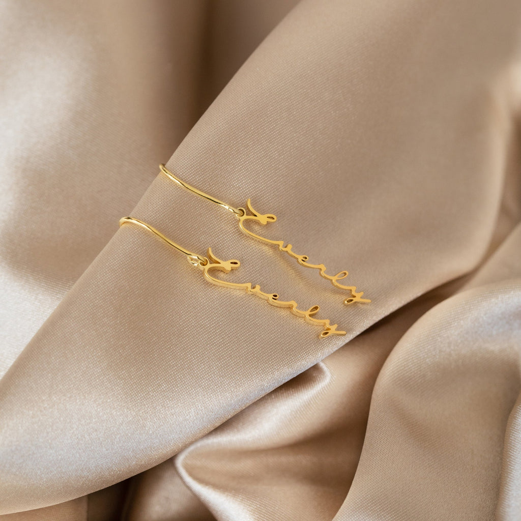 Minimal Dangling Name Earrings spelling Everly are displayed on beige satin fabric—an ideal, unique gift for bridesmaids.