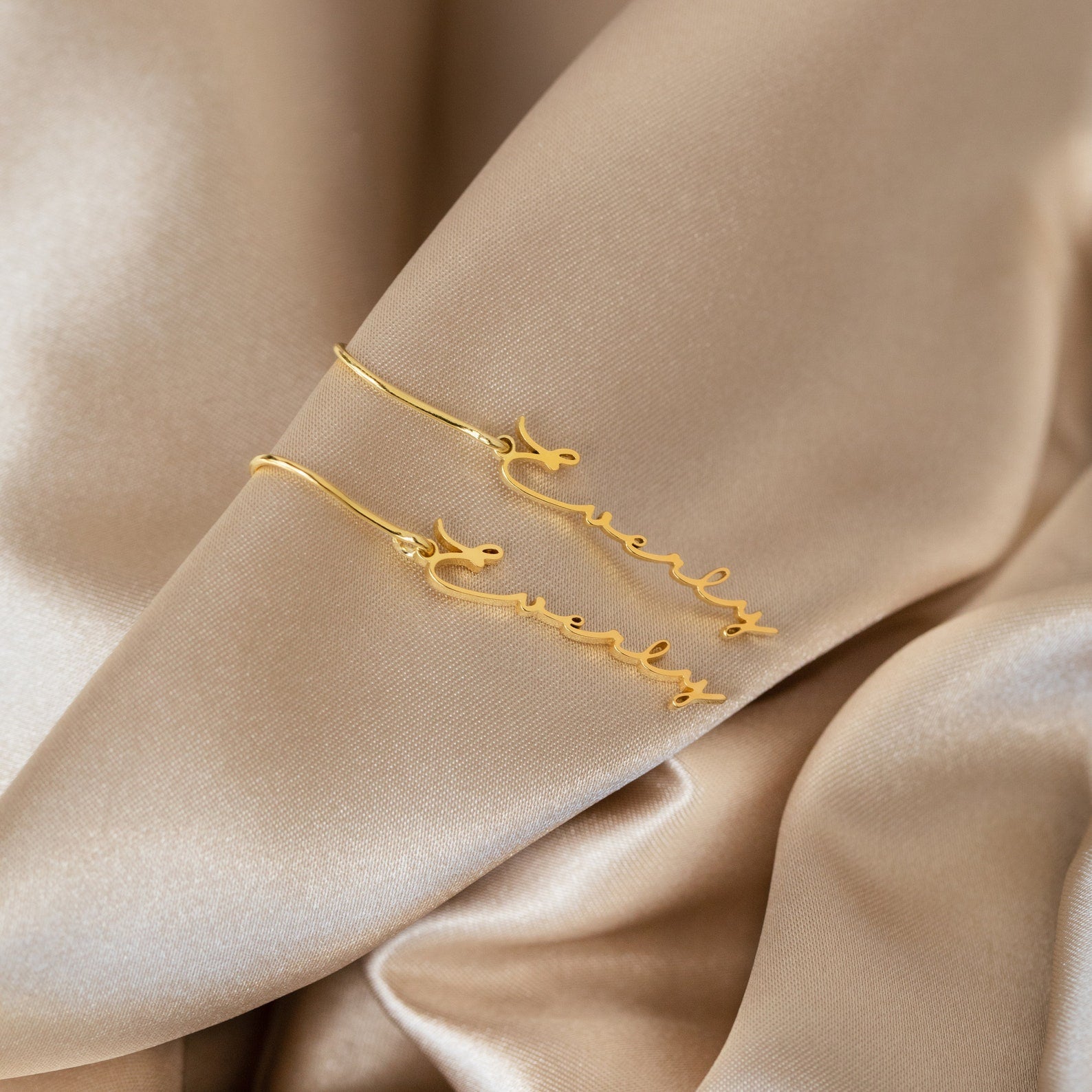 Minimal Dangling Name Earrings spelling Everly are displayed on beige satin fabric—an ideal, unique gift for bridesmaids.