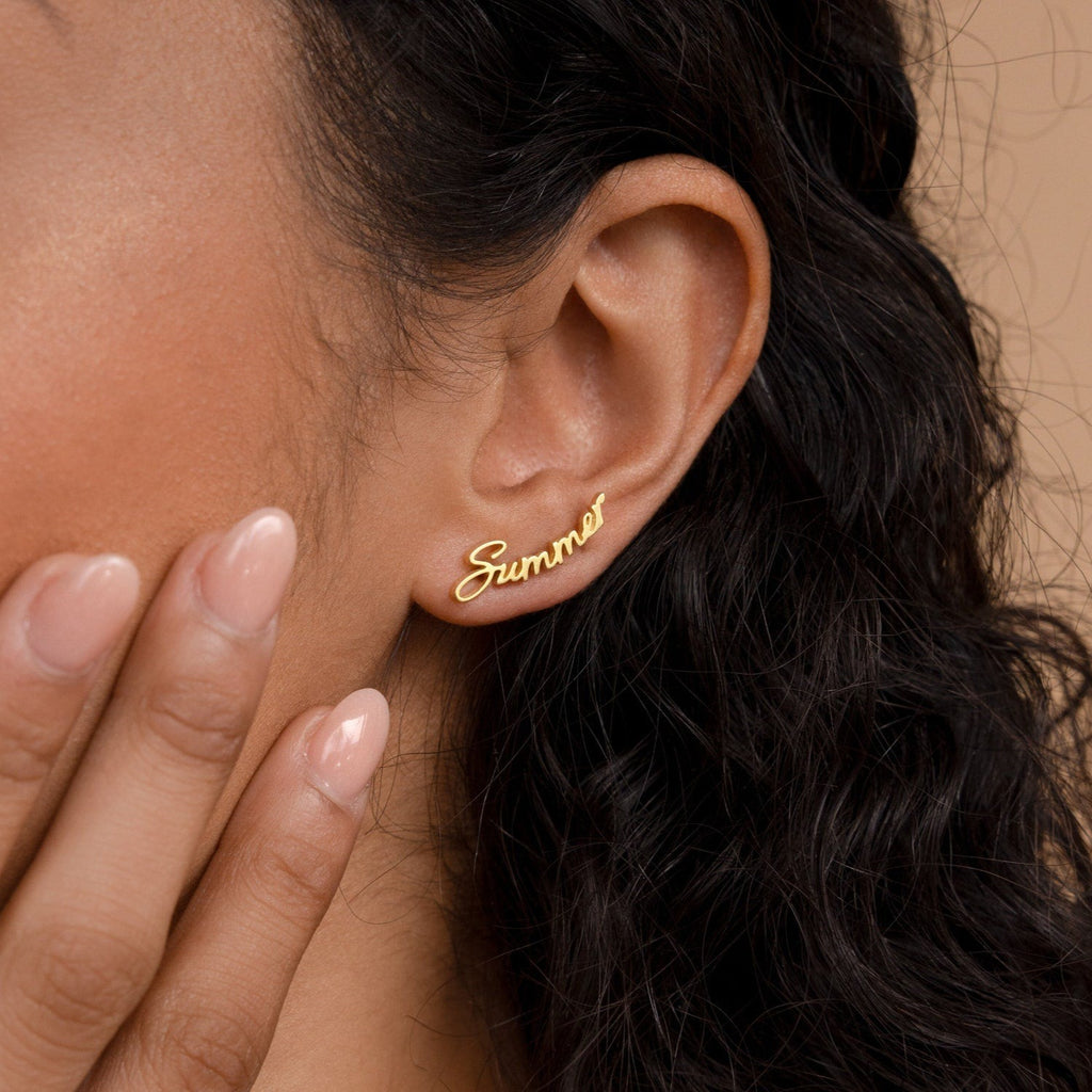 A Grace Name Earring spelling "summer" shines on a woman's ear as she gently touches her cheek—the perfect personalized earring and custom gift.