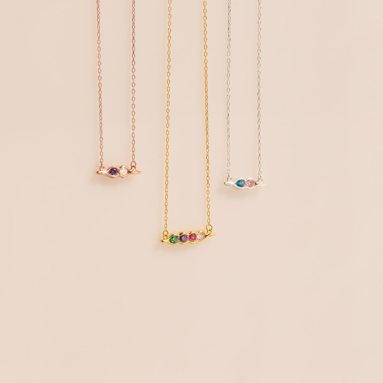 The Horizontal Pod Birthstone Necklace is shown with various colored chains on a beige background—ideal for anyone wanting a personalized jewelry accent or a custom birthstone necklace.