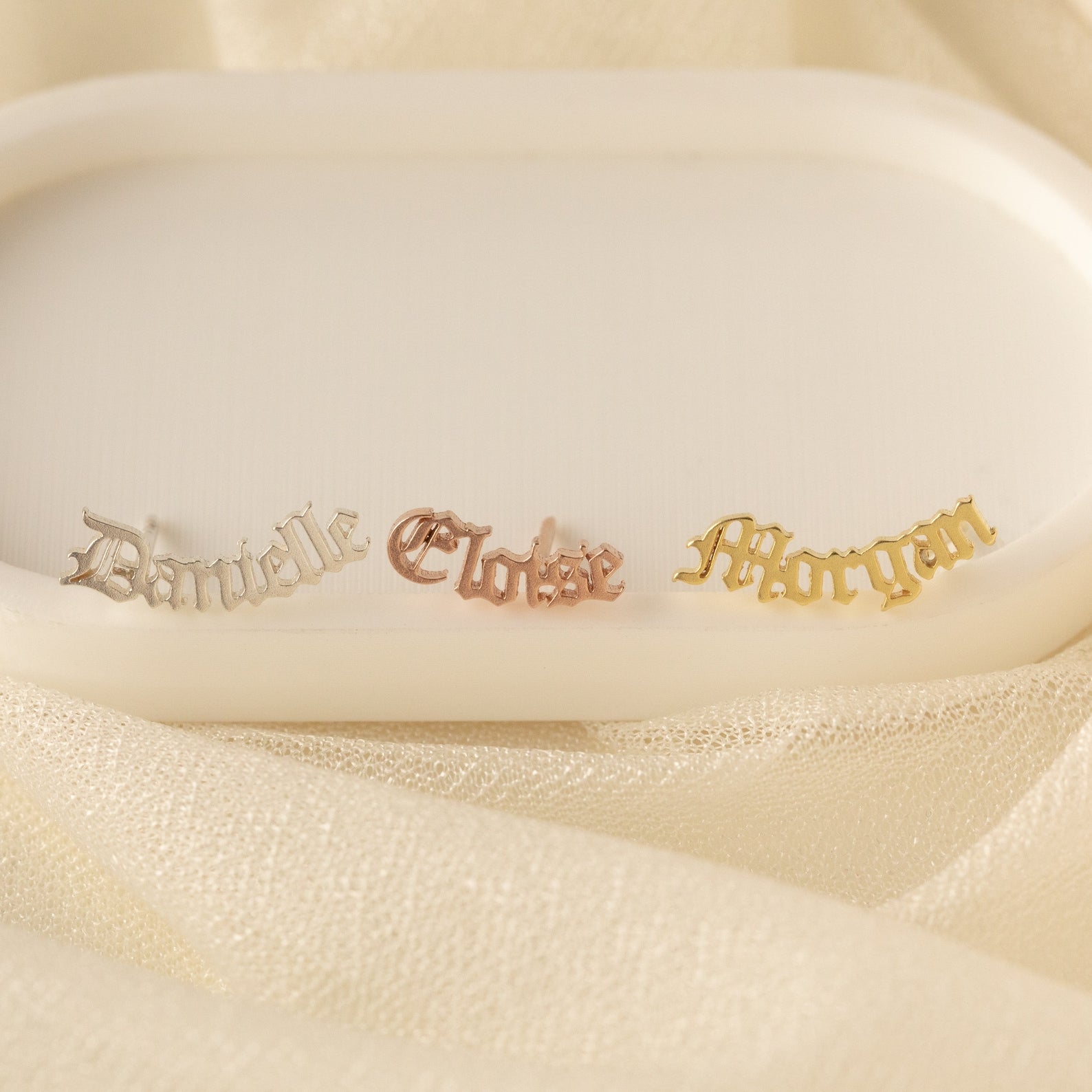 Old English Name Earrings: white rectangular display with gold and silver name tags, ideal for custom gifts or personalized inspiration.