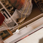 The Ariel Pearl Necklace features a gold chain with a delicate pearl pendant, displayed on vintage photos and fabric—perfect as bridal jewelry or a thoughtful bridesmaid gift.