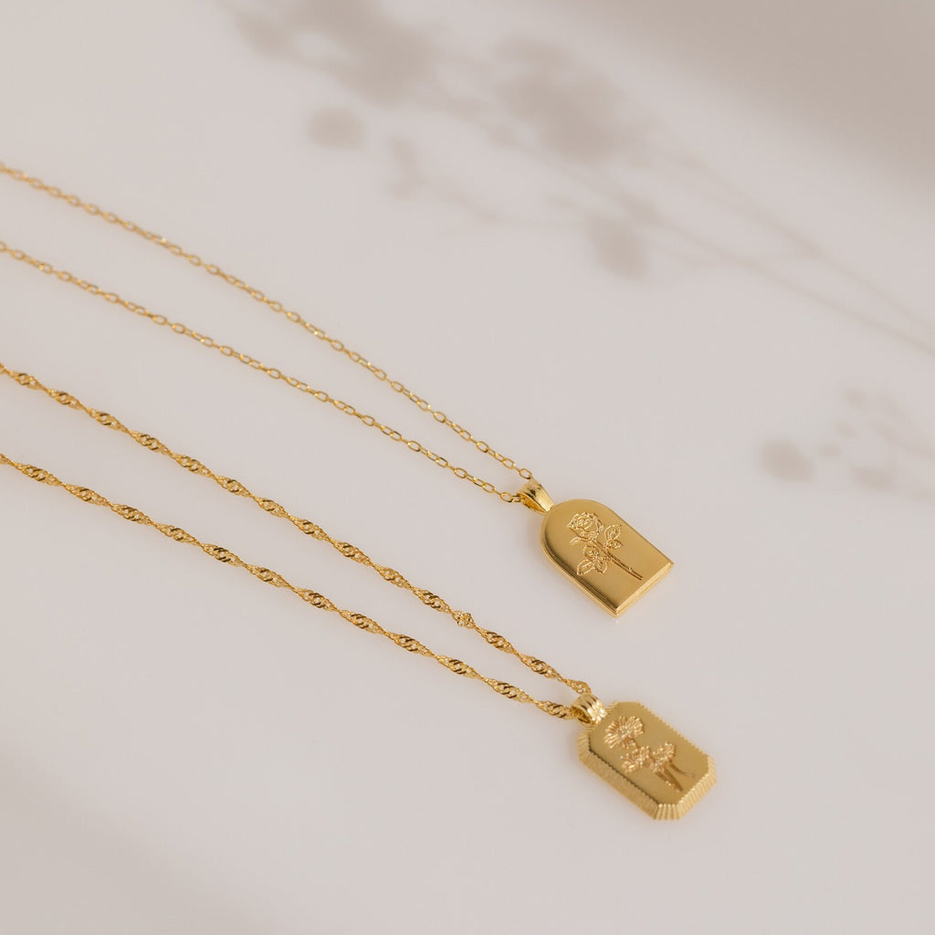 Two Birth Flower Arch Necklaces with delicate chains rest on a neutral background with soft floral shadows—perfect personalized jewelry or a cherished birth flower necklace.