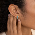 Close-up of a person touching their ear, wearing Baguette Birthstone Bar Studs—small gold earrings featuring blue stones.