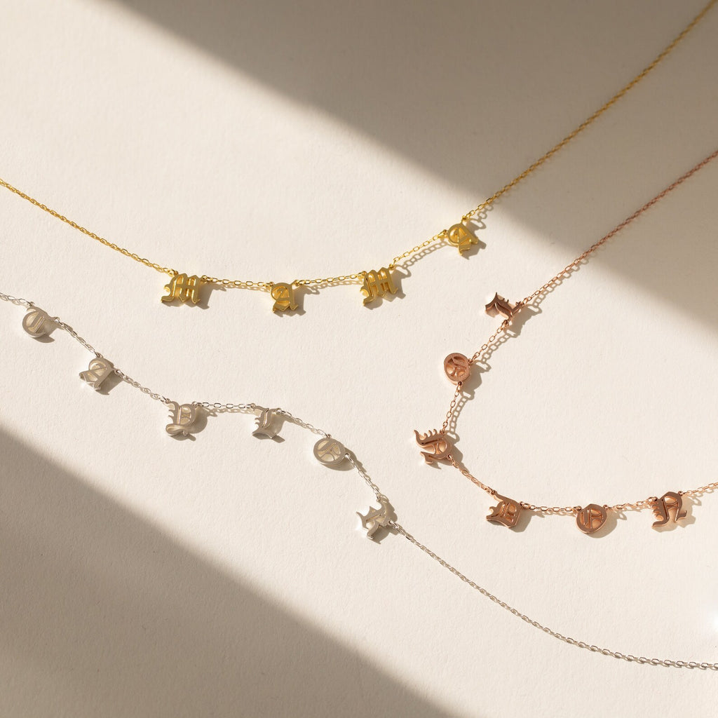 The Old English Letter Name Necklace, available in gold, silver, and rose gold finishes, is displayed on a light background—perfect for lovers of minimalist jewelry with a personalized touch.