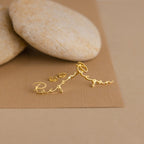 Gold personalized Hallie Name Earrings in cursive, shown on a brown background with smooth stones—ideal as a custom gift or unique name stud earrings.