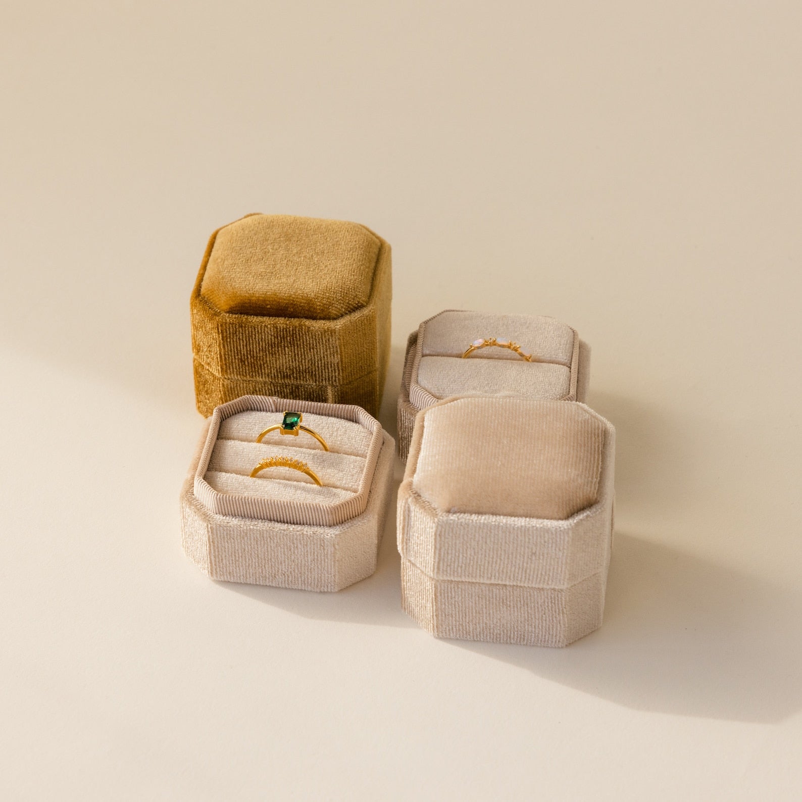 Three elegant 2 Slot Velvet Ring Boxes—two beige, one gold—showcase gold rings on a neutral background, with one box featuring a two-slot holder for added sophistication.