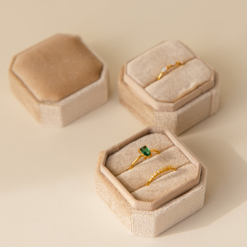 Three elegant 2 Slot Velvet Ring Boxes display gold rings—one with a green gemstone—on a neutral surface.