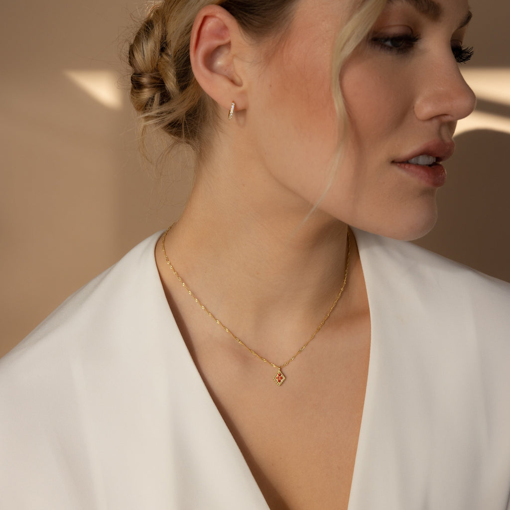 Woman in a white blouse wears a Birthstone Diamond Pendant Necklace and hoop earring, her hair styled in a loose updo.