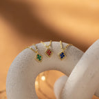 Three Birthstone Diamond Pendant Necklaces with green, red, and blue gemstone pendants are elegantly displayed on a curved white surface—perfect for anyone seeking unique, handmade gemstone jewelry.