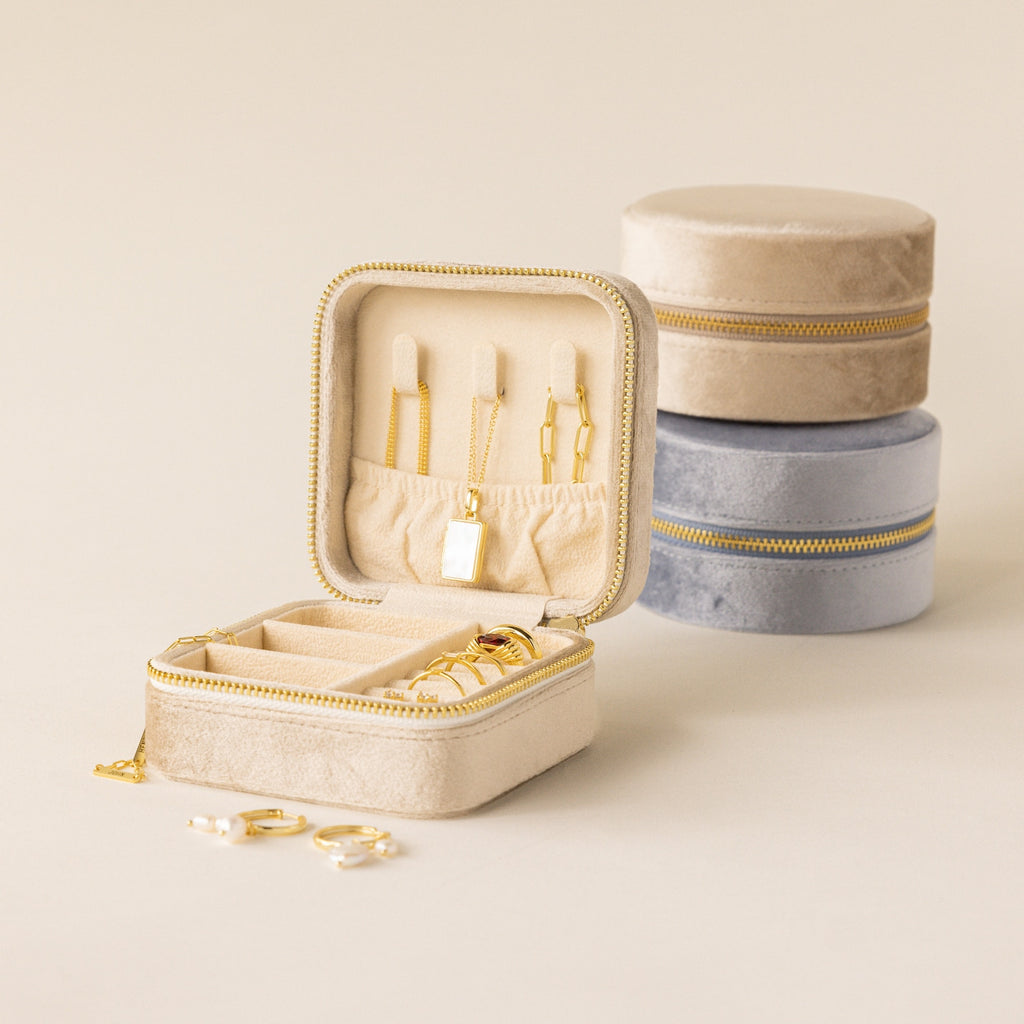 Square Velvet Jewelry Case in beige velvet, shown open with gold jewelry inside, placed next to closed beige and gray cases on a neutral background.