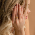 A blonde woman wears the Hallie Duo Initial Ring, featuring gold BN lettering on her finger while covering part of her face—an elegant, personalized jewelry piece.