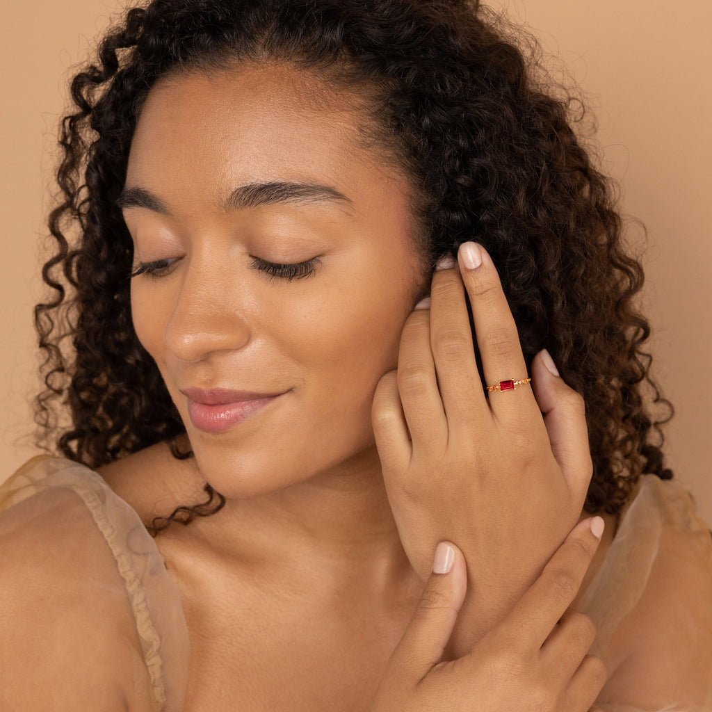 A woman with curly hair wearing a delicate Space Baguette Birthstone Ring in gold.