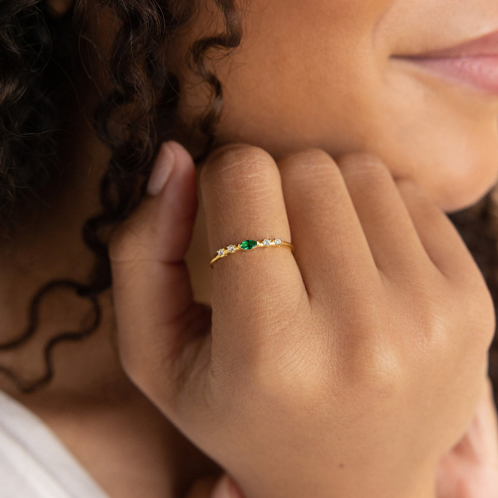 A woman smiles, wearing a Space Marquise Birthstone Ring adorned with green and clear crystals on her finger.