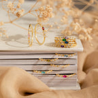 The Space Marquise Birthstone Ring, featuring customizable gemstones and colorful crystals, is displayed on stacked books with dried flowers in the background.