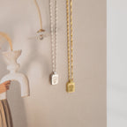 Silver and gold necklaces, including the Ribbed Flower Tag Necklace with engraved pendants, are displayed against a soft, neutral-toned background.