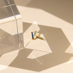 Baguette Birthstone Bar Studs with blue accents, ideal for ear piercing or as a stylish birthstone earring, presented on a beige surface with geometric glass shadows.