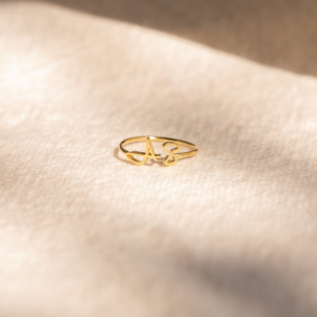The Hallie Duo Initial Ring, personalized with the letters A S, rests on a soft beige surface in gentle sunlight—the perfect gift for mothers who love meaningful jewelry.