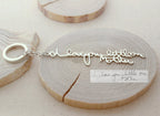 Custom Handwriting Keychain with "I love you little one Mother" engraved in silver, displayed on wood beside a handwritten note—a perfect keepsake for preserving special memories.