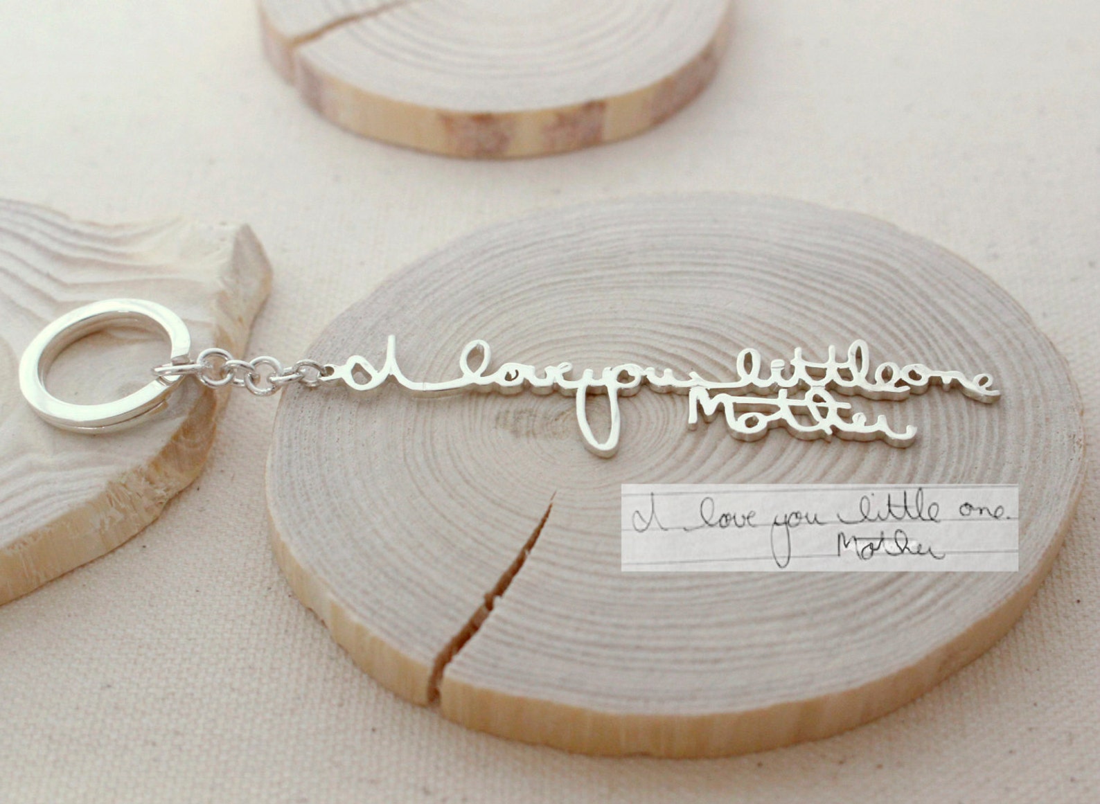 Custom Handwriting Keychain with "I love you little one Mother" engraved in silver, displayed on wood beside a handwritten note—a perfect keepsake for preserving special memories.