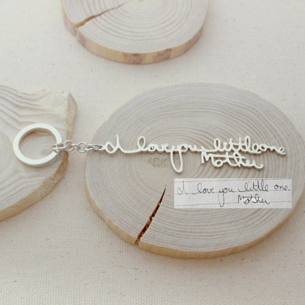 The Custom Handwriting Keychain features "I love you little one Mother" in script, replicating the handwritten note beside it—a perfect way to turn your handwriting into unique jewelry.