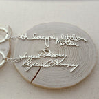 Showcasing two silver necklaces with cursive handwriting pendants on wood; one says "I love you little one Mother." These unique pieces pair perfectly with our Custom Handwriting Keychain—ideal for heartfelt, personalized gifts.