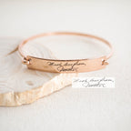 The Handwriting Bar Bangle in rose gold showcases "Much love from, Mother" engraved in elegant cursive—a stunning piece of personalized jewelry with your custom handwriting.