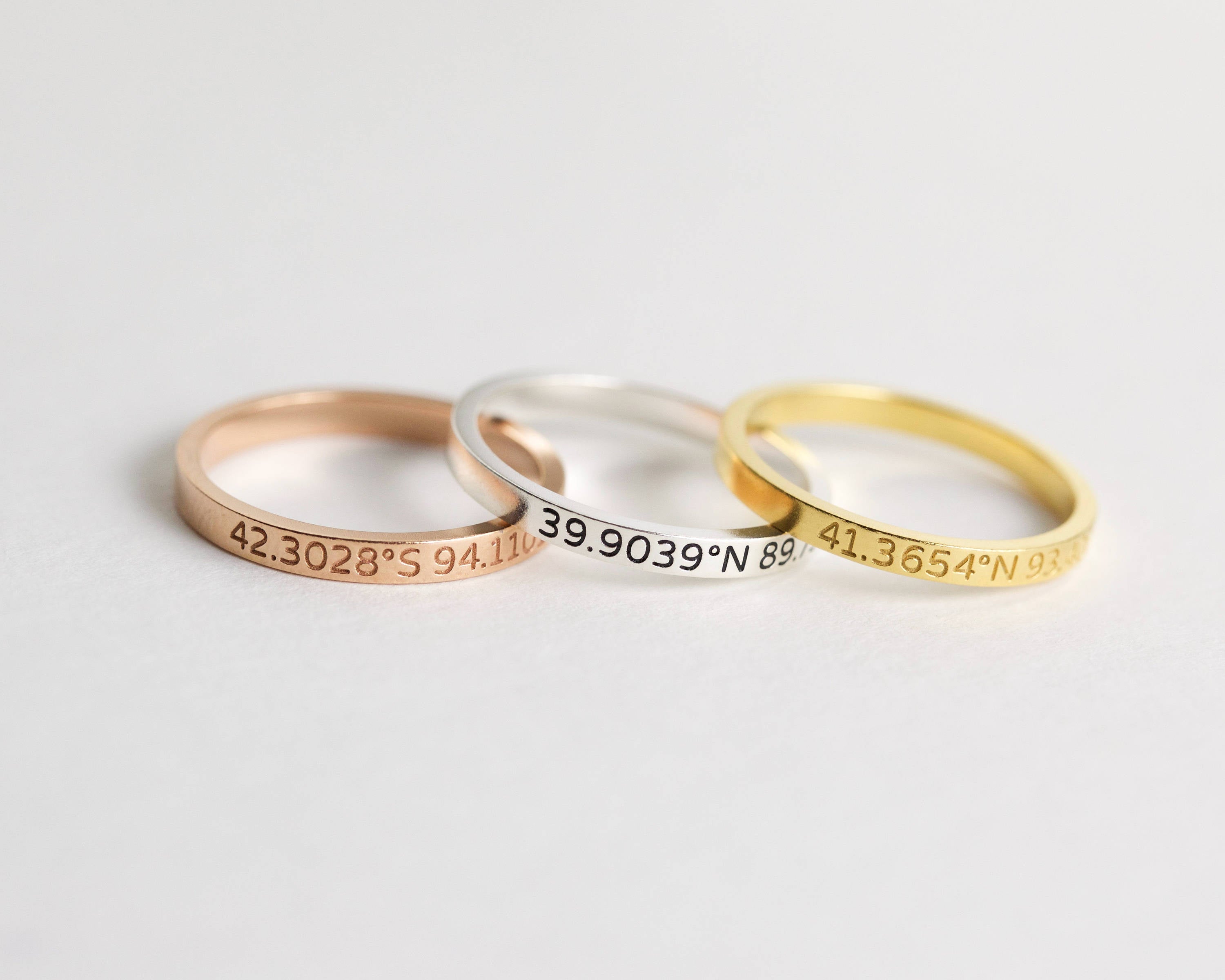 The Coordinates Band features three metal stacking rings—rose gold, silver, and gold—engraved with geographic coordinates to capture a meaningful memory.